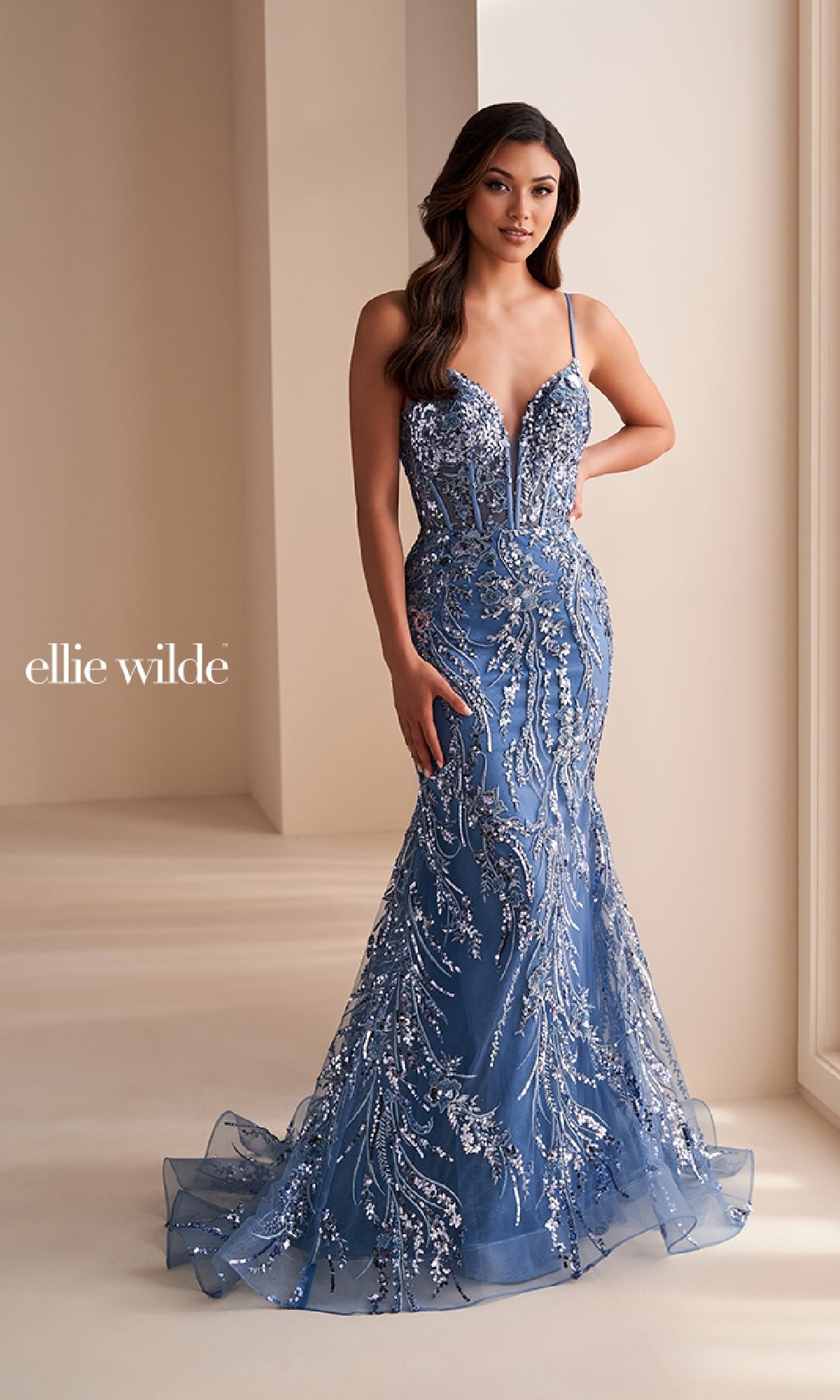Woman wearing the Ellie Wilde Long Black Sequin Prom Dress EW35039, a floor-length mermaid gown with sleeveless design and silver sequin embellishments, standing indoors near a window.